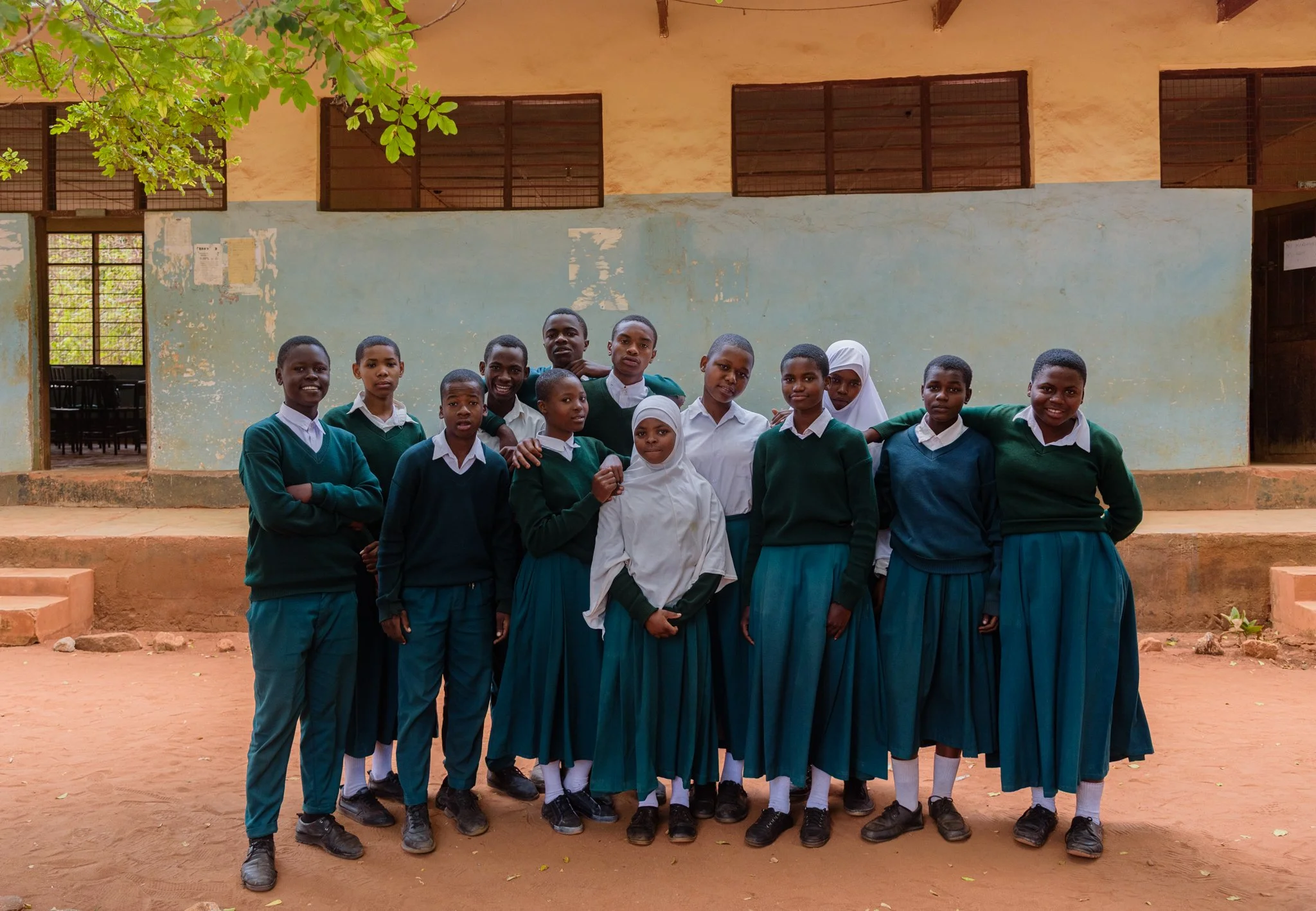 Group of primary school students in uniform standing outdoors in front of a school building in Tanzania, photographed during a Malala Fund assignment on girls’ education.