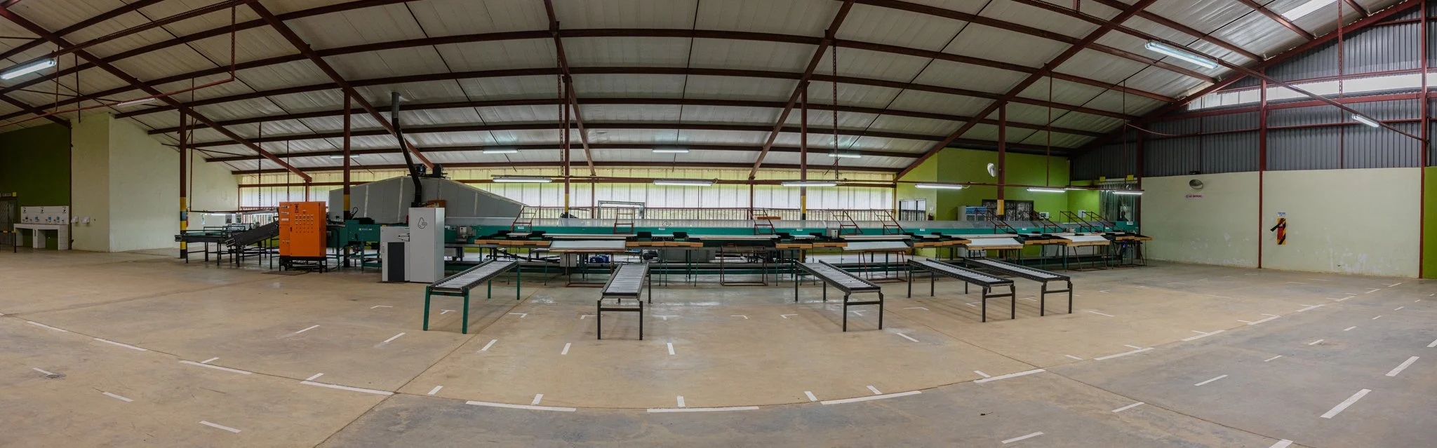 Interior of a large warehouse or factory with a metal roof, open floor space, and industrial equipment in the background. In Mbeya, Tanzania.