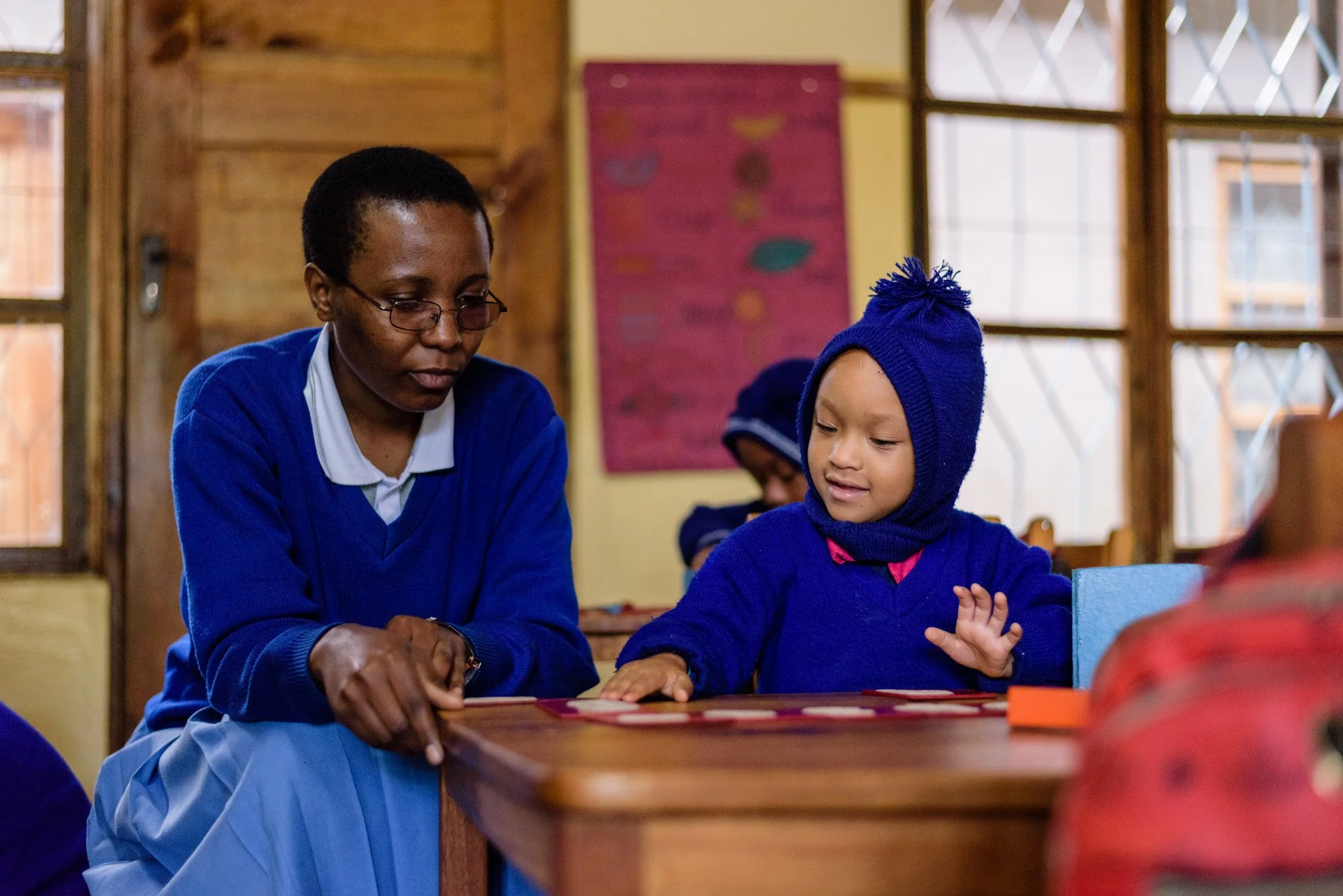 Teacher at a Montessori kindergarten in Lushoto guiding a young student in arranging numbers during a classroom learning activity in Lushoto, Tanga Region, Tanzania.