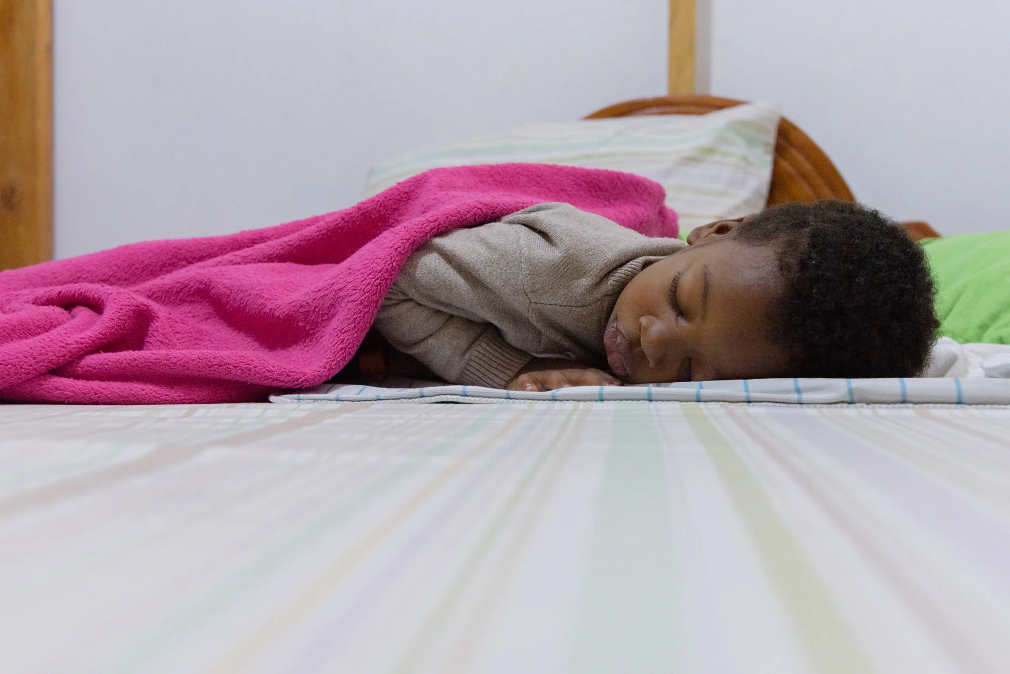Young child sleeping on a bed with a colourful striped bedspread and blanket in Mwanza, Tanzania.