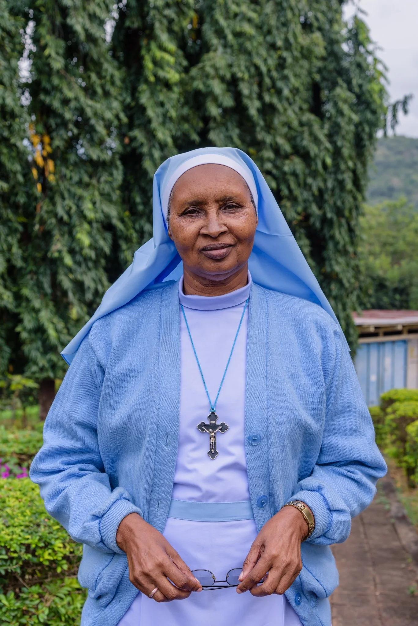 Portrait of a Catholic nun holding eyeglasses, standing outdoors at the Usambara Sisters Convent in Korogwe, Tanzania.