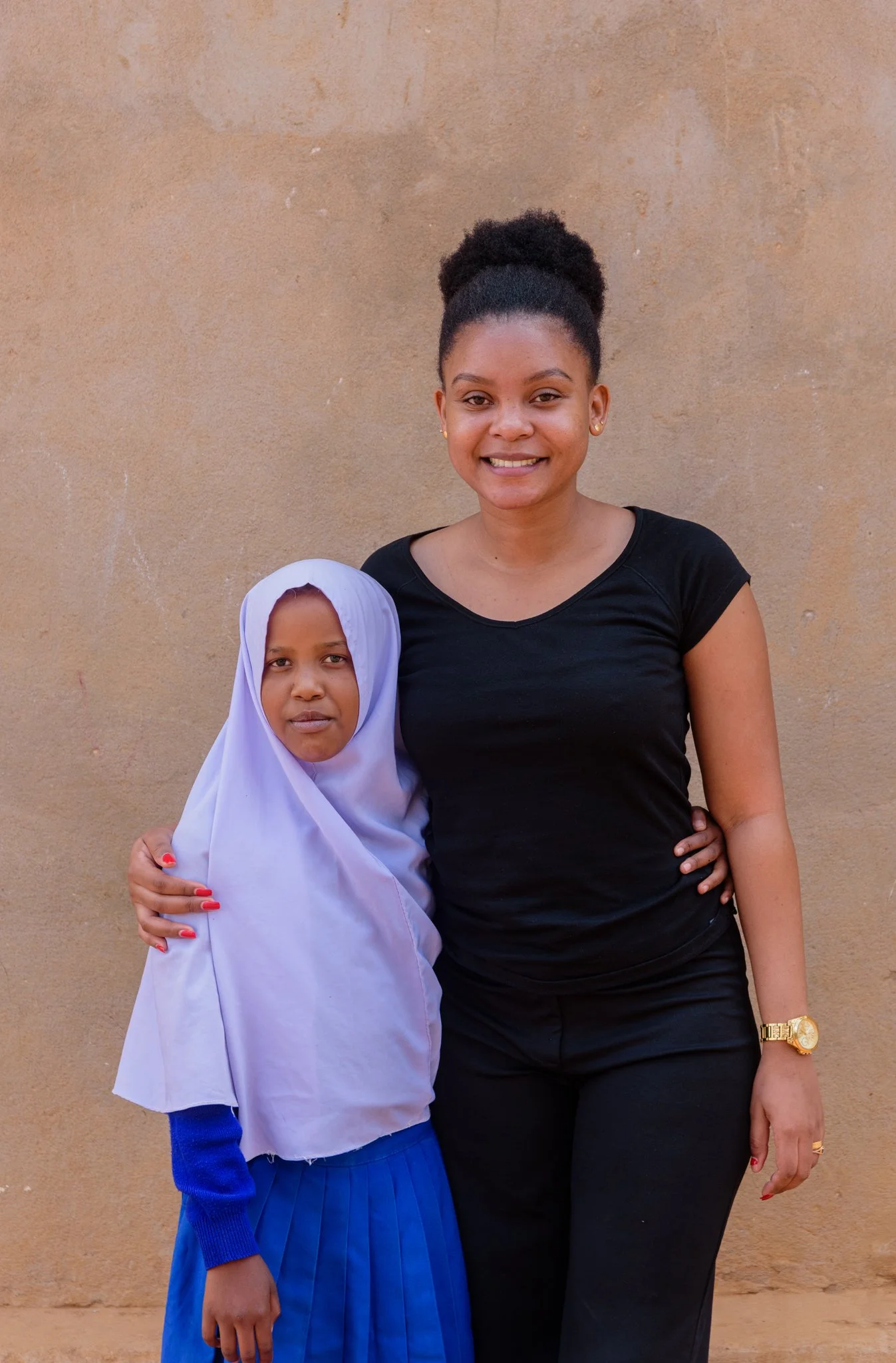 Tanzanian schoolgirl with Malala Fund champion, outdoors in school uniform and headscarf.
