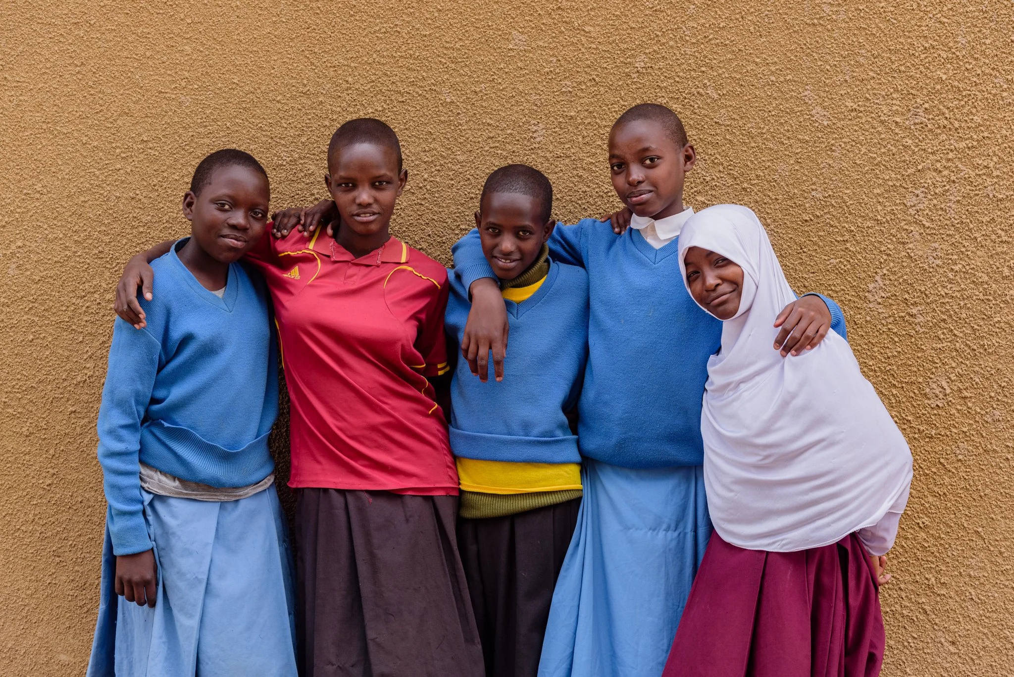 Five Tanzanian secondary schoolgirls smiling together in front of a wall in Arusha, Tanzania.