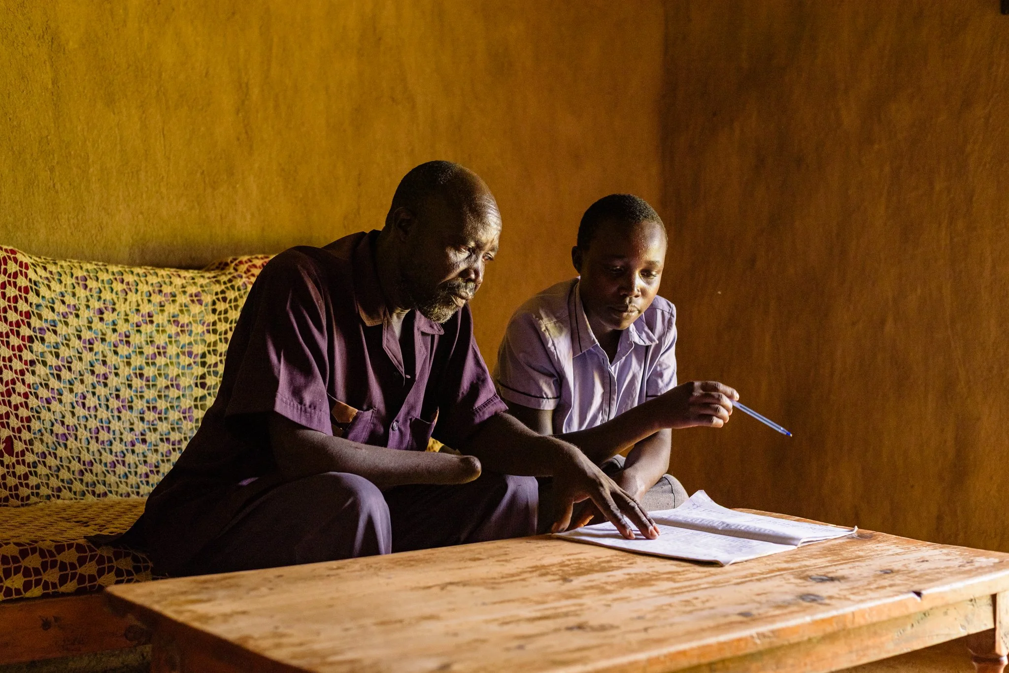 Father teaching his child indoors at their home in Kenya as part of an inclusive education initiative supported by Leonard Cheshire.