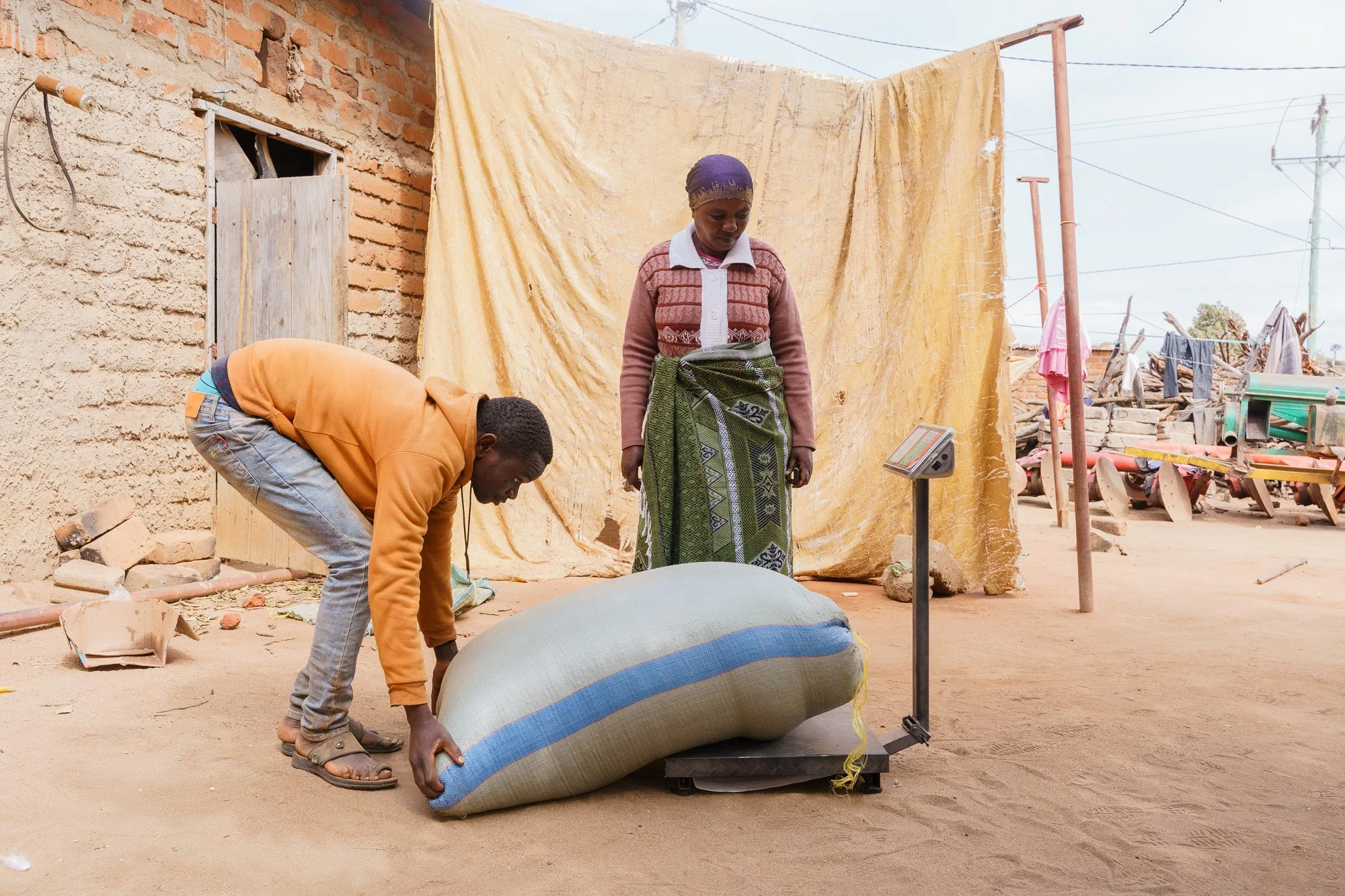 Two people weighing a large bag on a scale outdoors during a Farm Africa assignment in Babati, Manyara, Tanzania.
