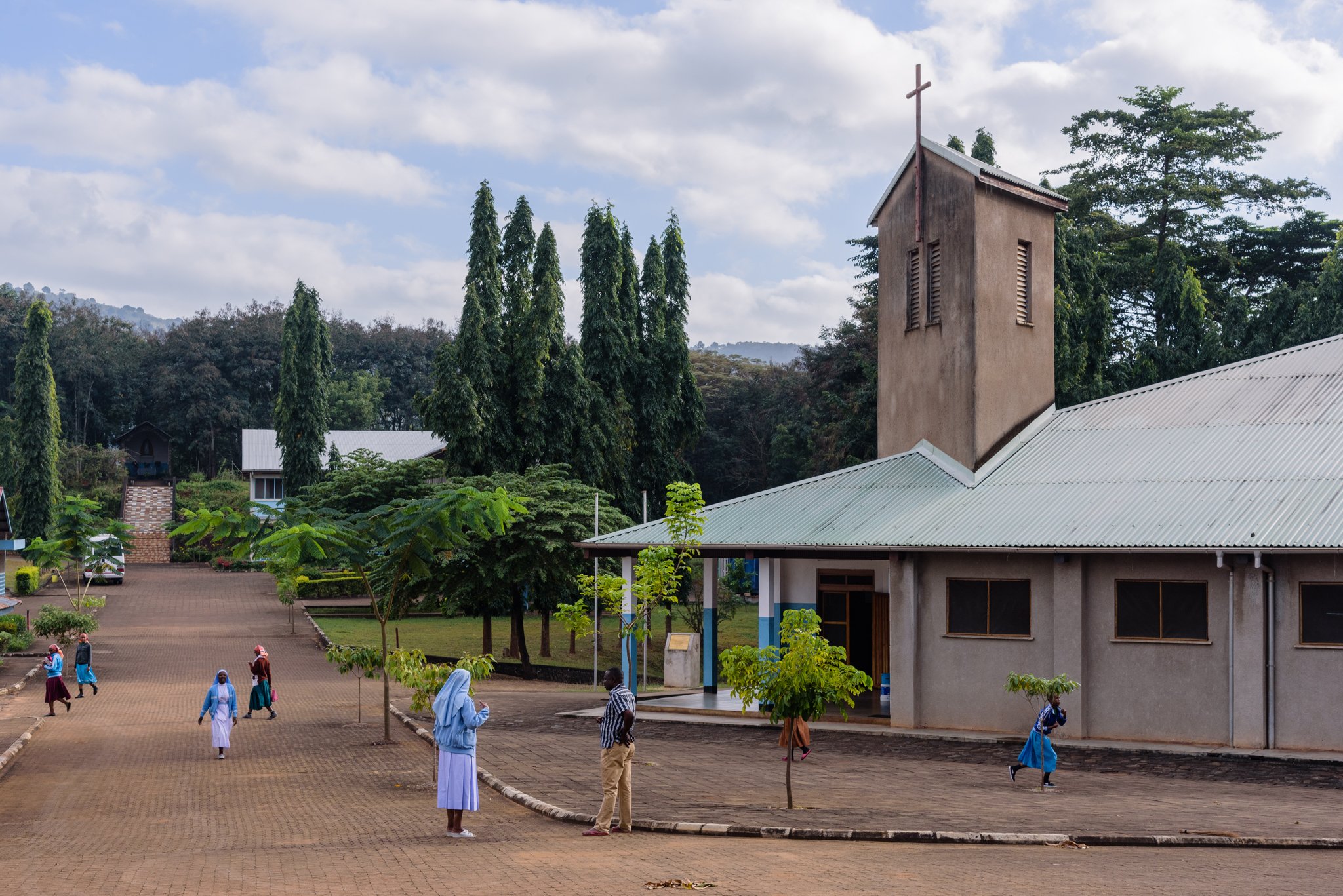Exterior view of a Usambara Sisters convent compound surrounded by trees and hills in Korogwe, Tanzania.