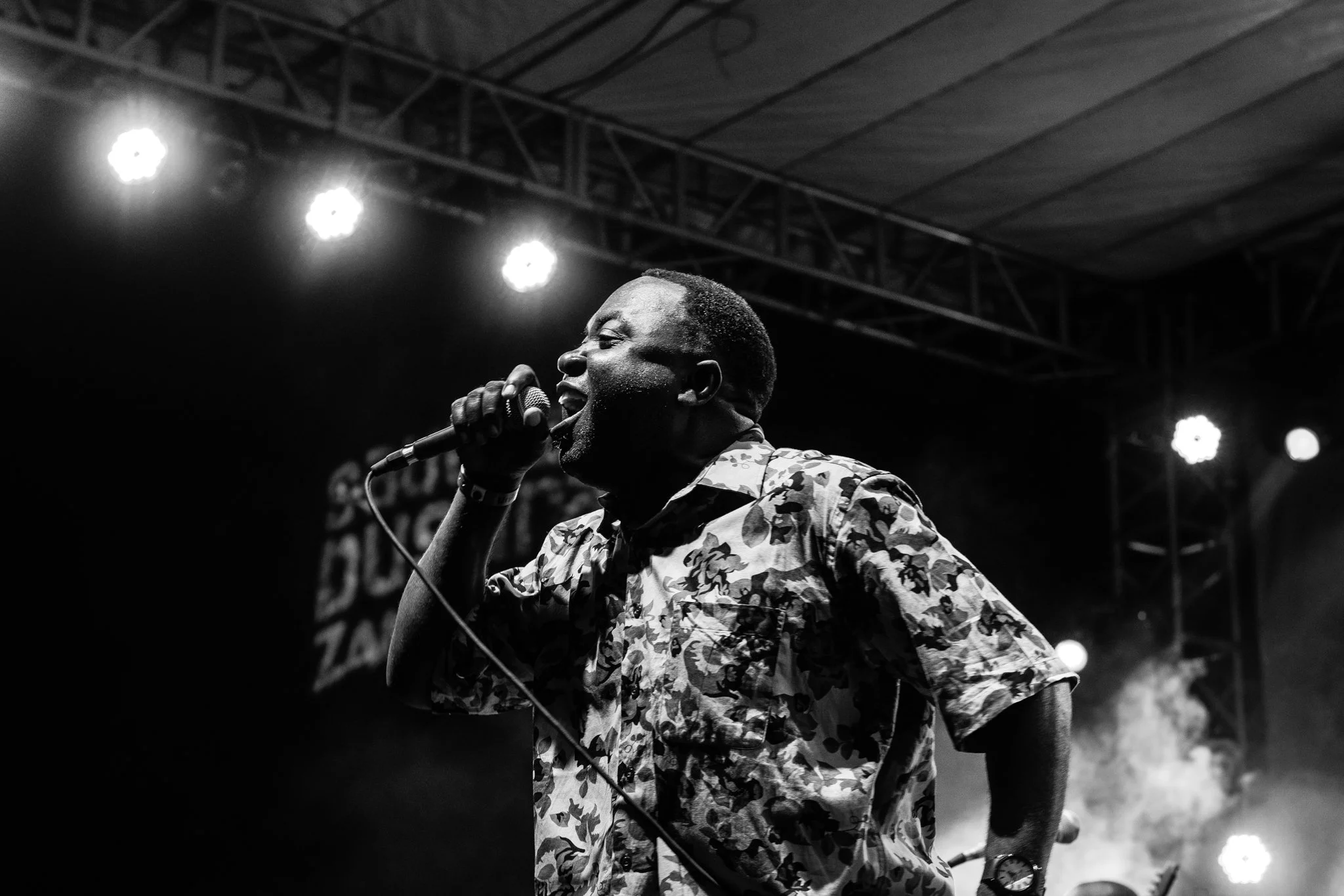 A man singing passionately into a microphone on stage with stage lights and smoke in the background in Zanzibar at the Sauti za Busara Music Festival in 2018.