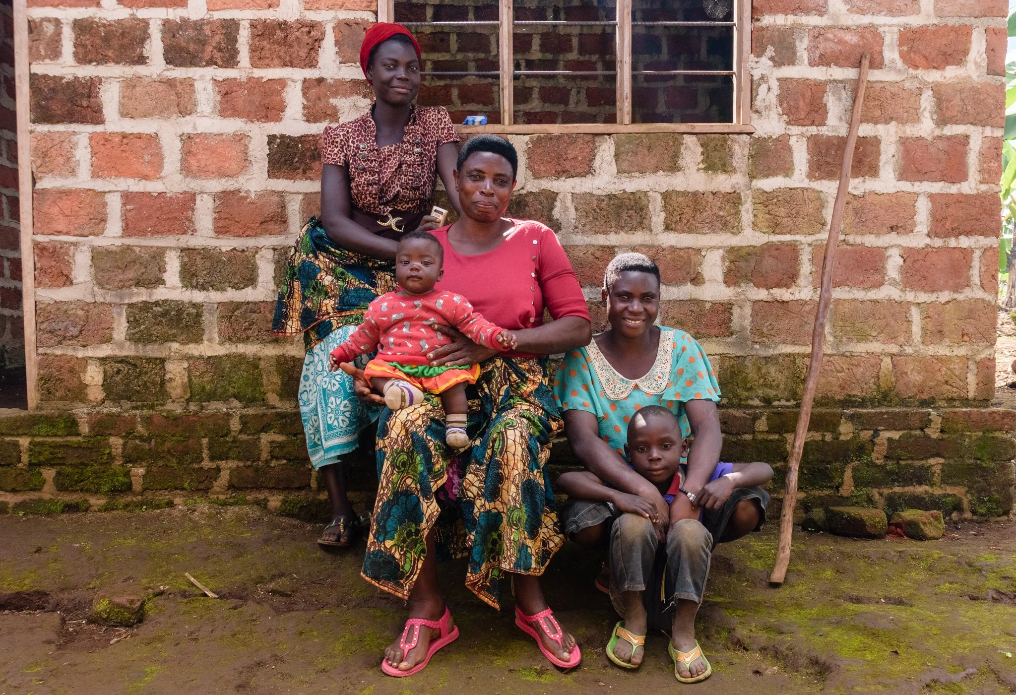 Documentary family portrait of four women and two children gathered outside a mud brick house in Mbeya, Tanzania.