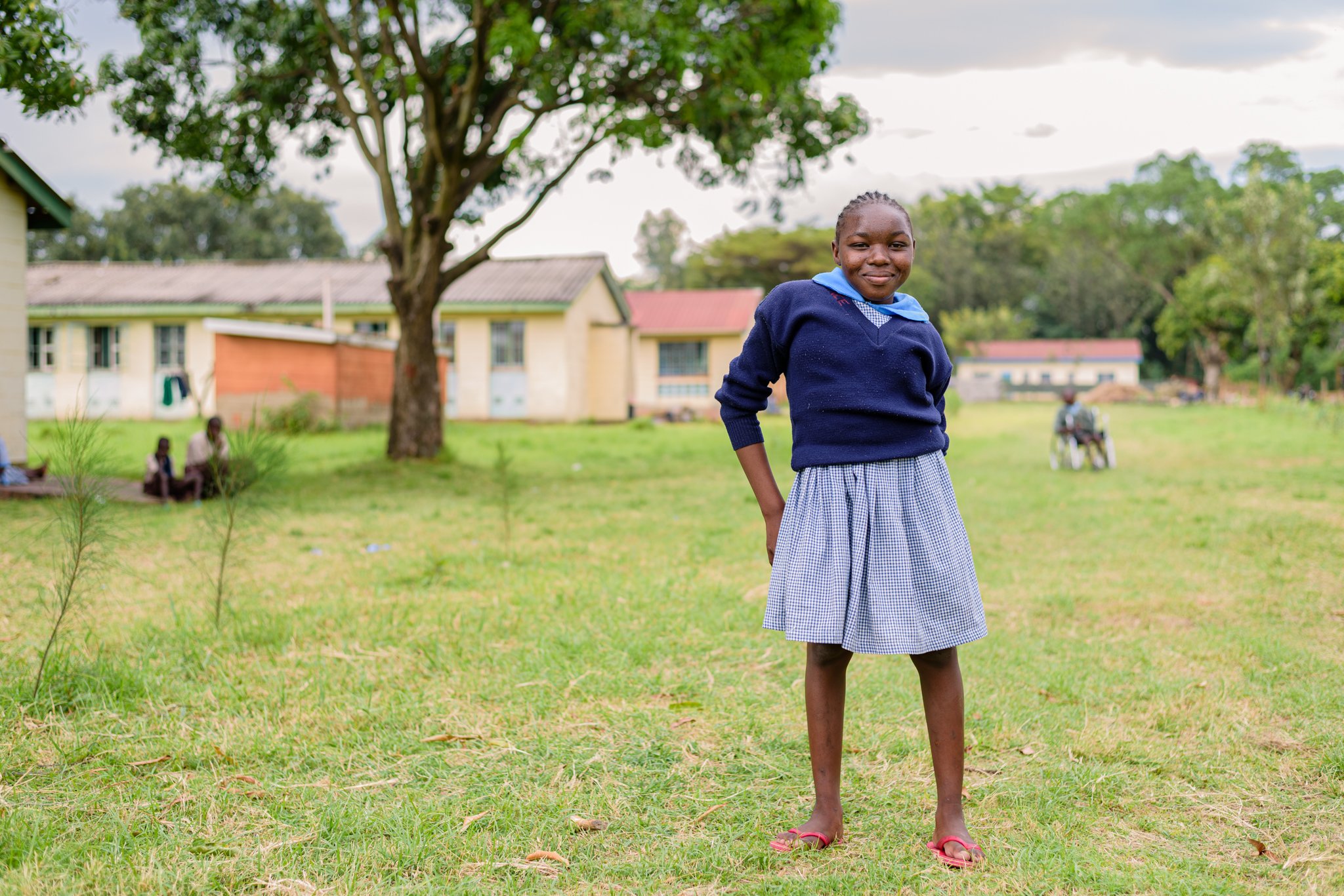 Portrait of a schoolgirl standing in a school field in Kenya, participating in an inclusive education programme supported by Leonard Cheshire.