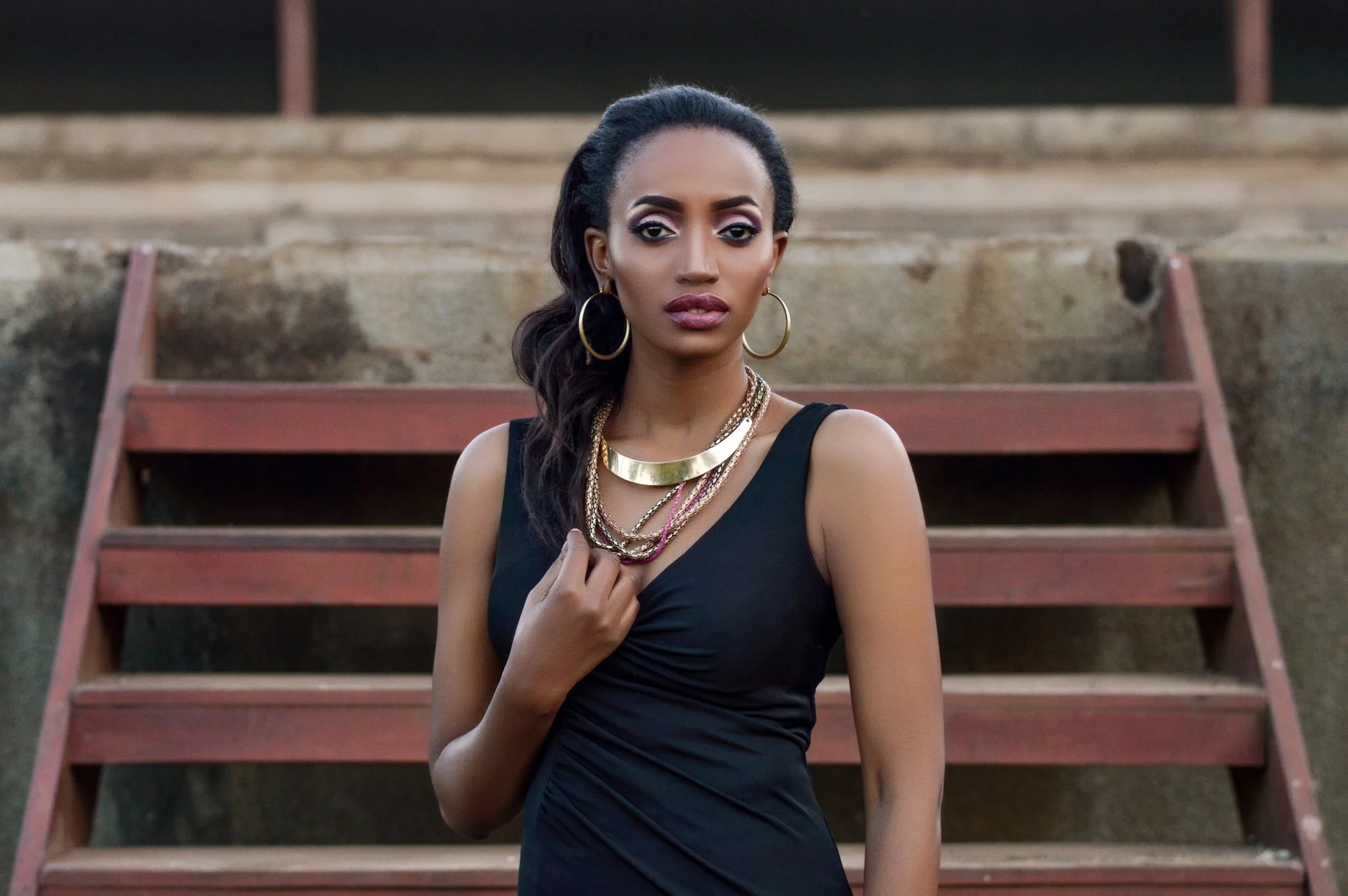 A woman in a black dress standing outdoors on a set of wooden stairs with purple spend and concrete stairs behind her.