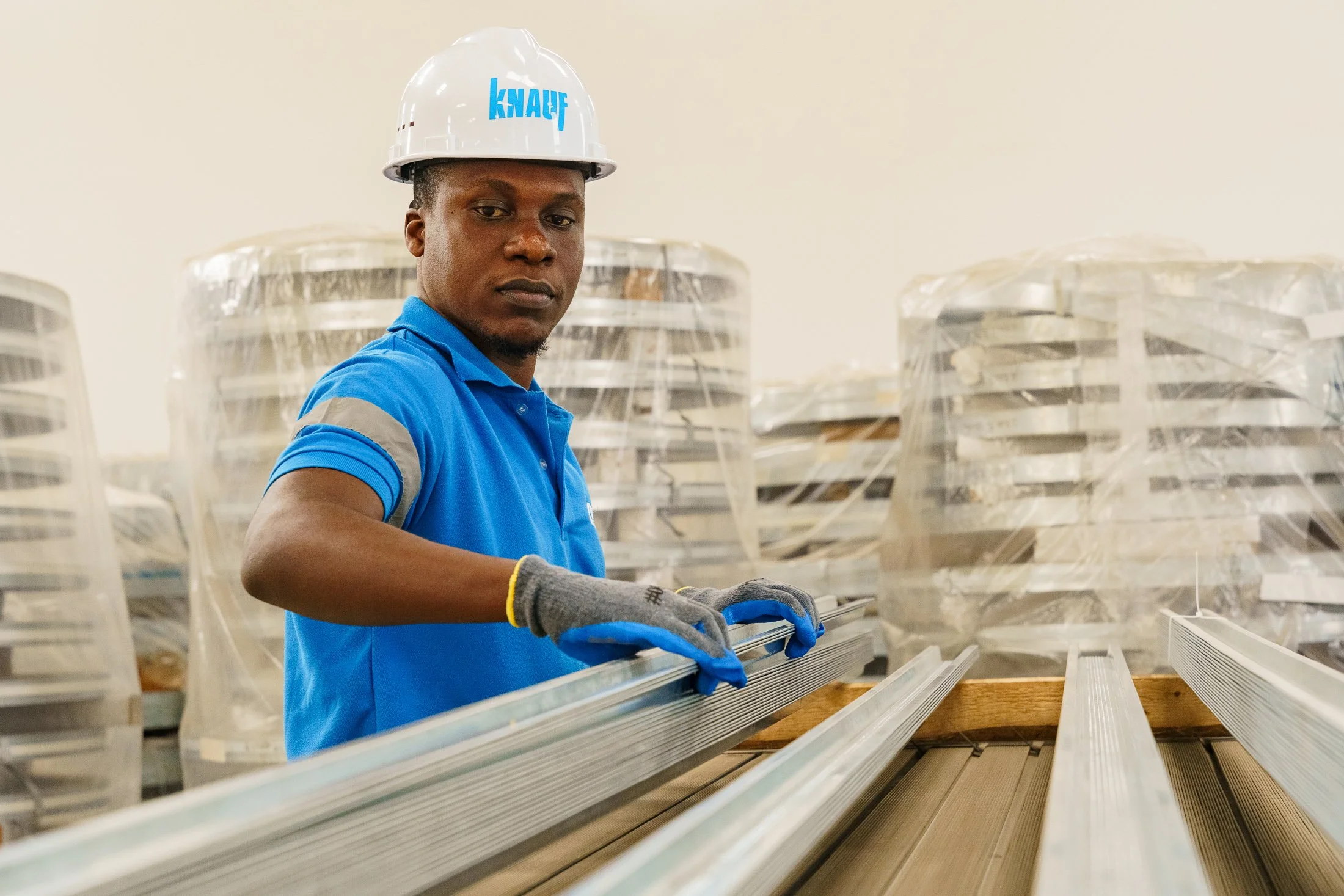 Factory worker wearing safety equipment handling construction profiles on a production line