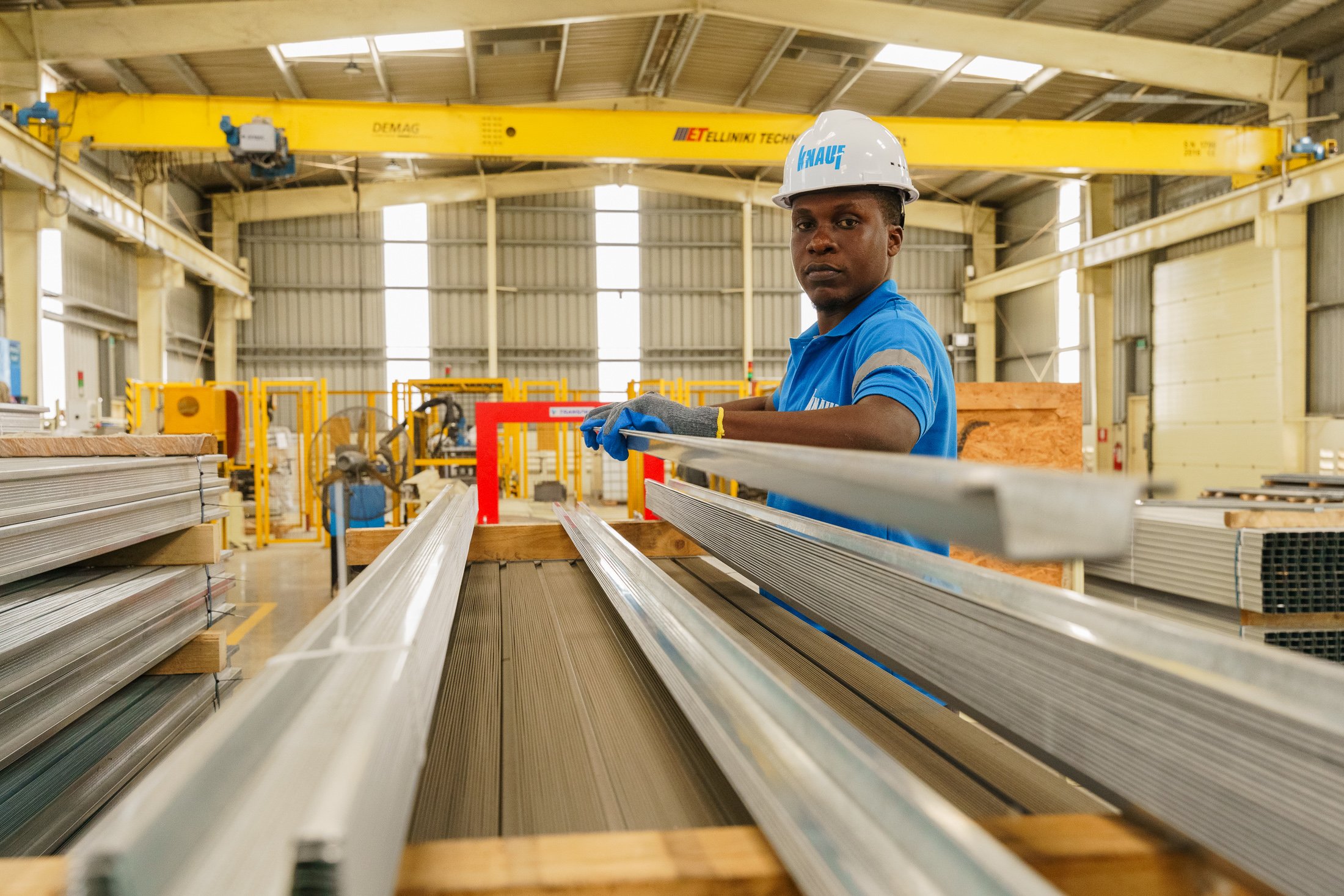 Long production line with construction materials and a worker inspecting output inside a factory