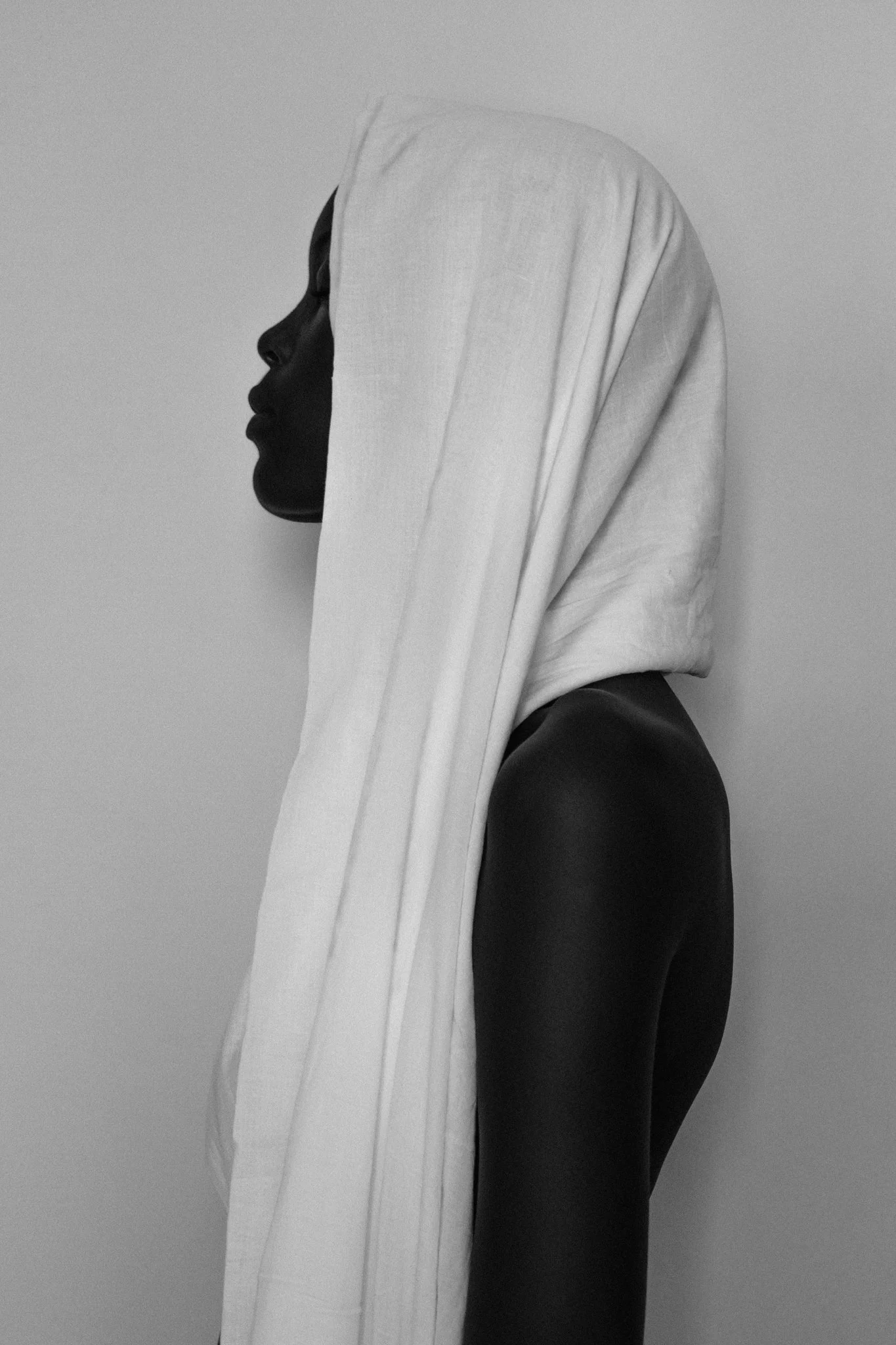 A high-contrast, black-and-white fine art side-profile portrait of a female model wearing a white headscarf against a plain background was captured in Dar es Salaam, Tanzania.
