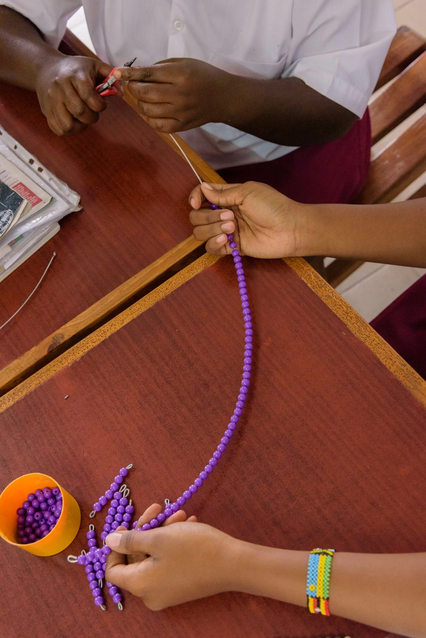 Hands of students at a Montessori Training Centre in Mwanza, Tanzania, during a practical session making beads to be used as teaching materials.