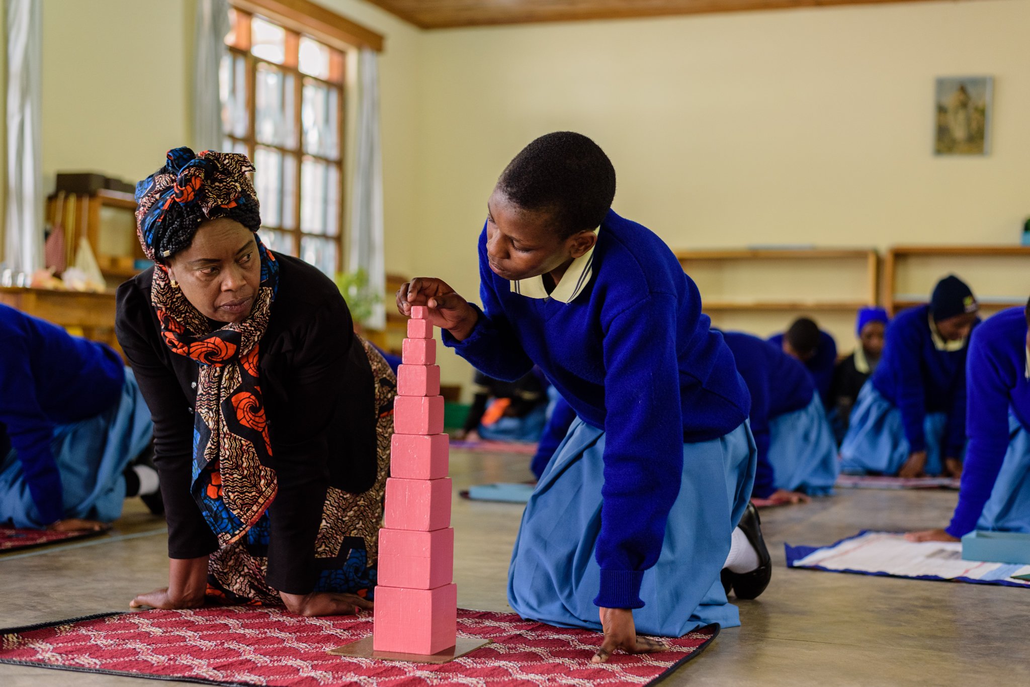 Teacher at the Montessori Training Centre in Lushoto instructing a trainee teacher on how to use handmade educational tools during a practical training session in Lushoto, Tanga Region, Tanzania.