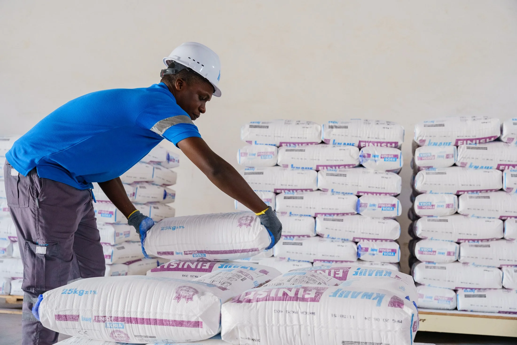 Worker stacking packaged construction materials inside an industrial warehouse in Mkuranga