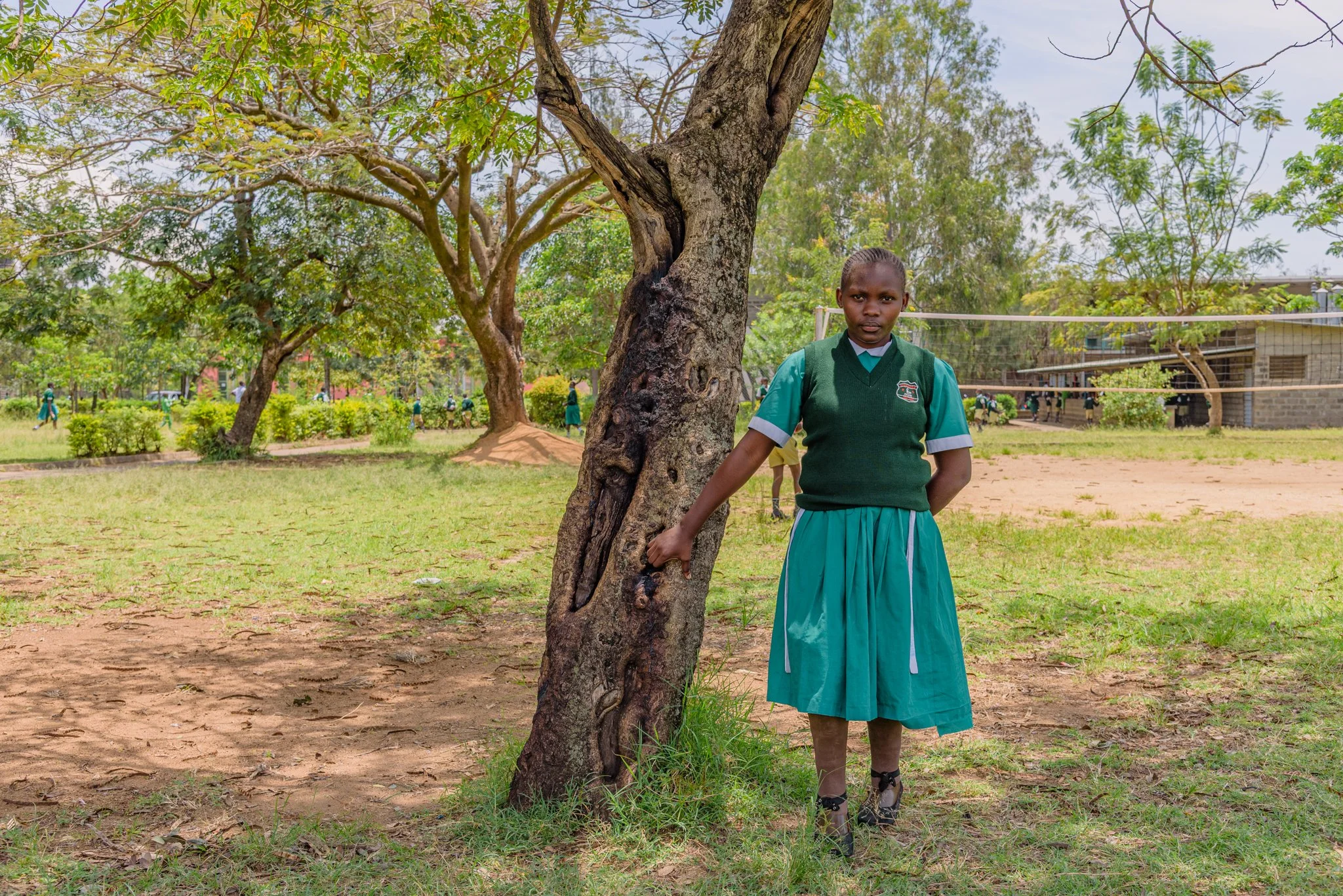 Schoolgirl standing near a tree on school grounds in Kenya, part of an inclusive education project commissioned by Leonard Cheshire.
