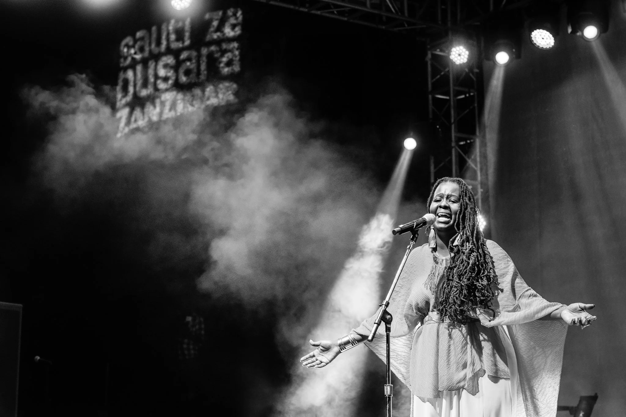 A woman with long dreadlocks singing into a microphone on stage with spotlights and fog effects in the background at the Sauti za Busara Music Festival 2018 in Zanzibar, Tanzania.