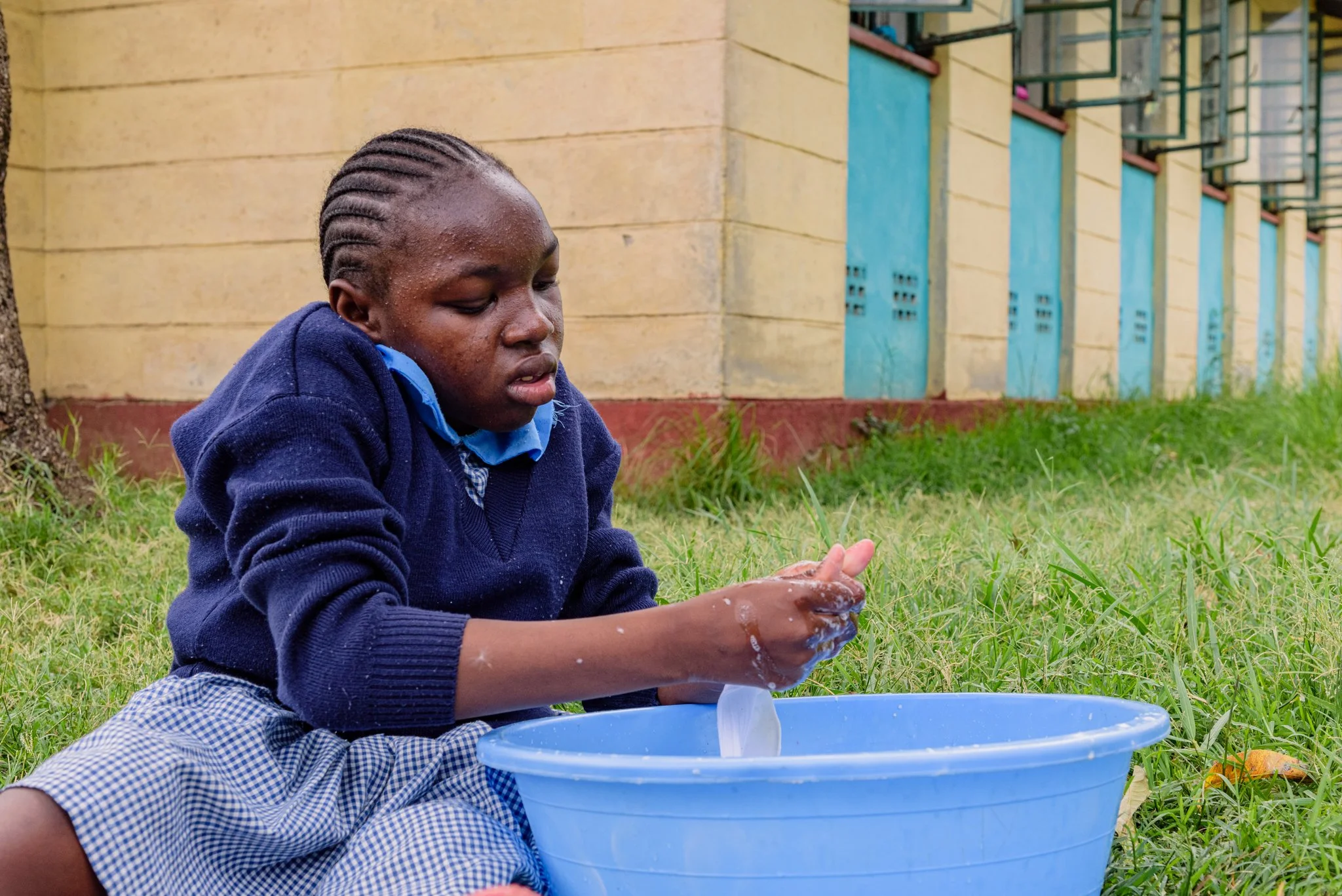 Schoolgirl washing her socks in a basin outdoors at a primary school in Kenya, participating in an inclusive education programme supported by Leonard Cheshire.