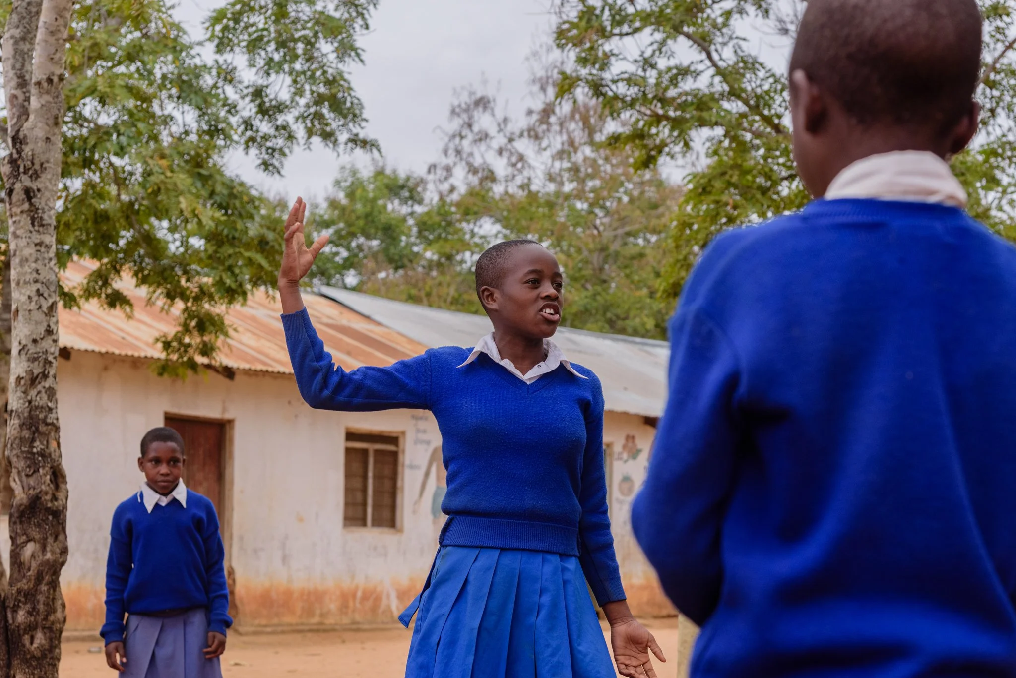 Primary school student in a blue uniform addressing two younger girls outside a school in Dodoma, Tanzania, captured during a Malala Fund assignment on girls’ education.