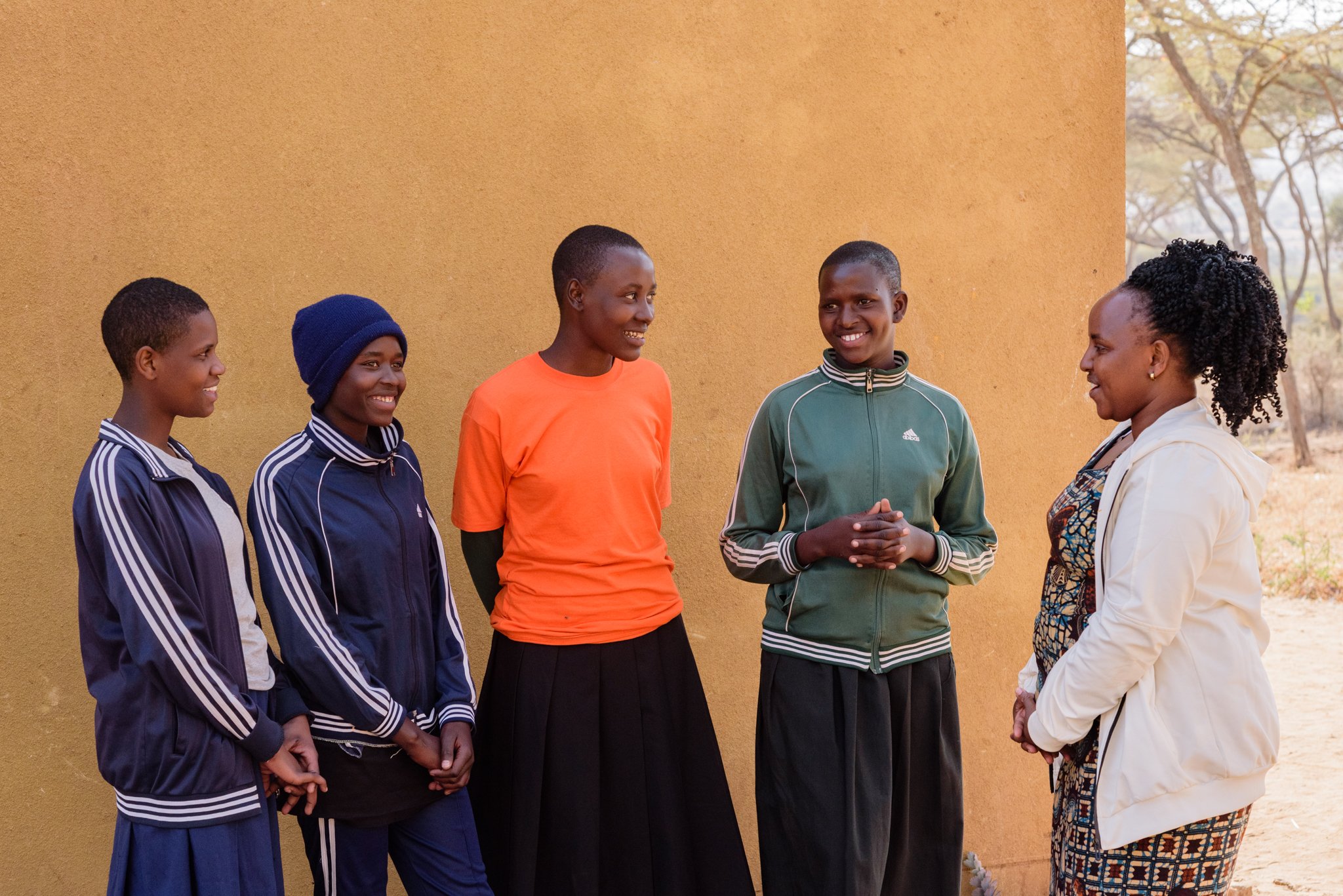 Malala Fund Champion standing outdoors with four Tanzanian secondary schoolgirls, smiling and having a casual conversation in Arusha, Tanzania.