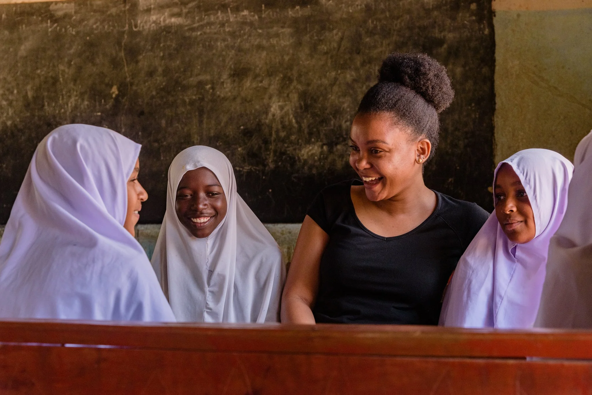 Malala Fund Education Champion sitting with four Tanzanian schoolgirls, two in white hijabs, smiling in Dodoma, Tanzania