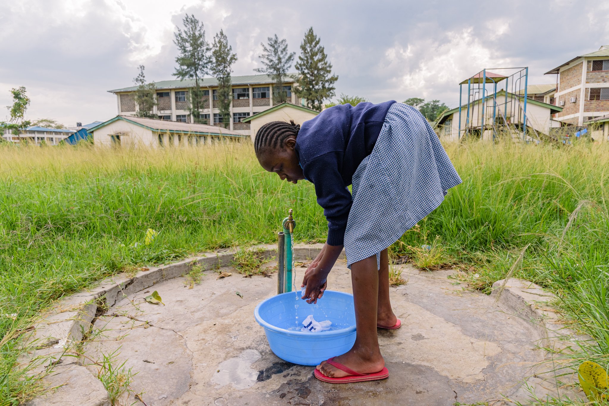 Schoolgirl washing her socks in a basin outdoors at a primary school in Kenya, participating in an inclusive education programme supported by Leonard Cheshire.
