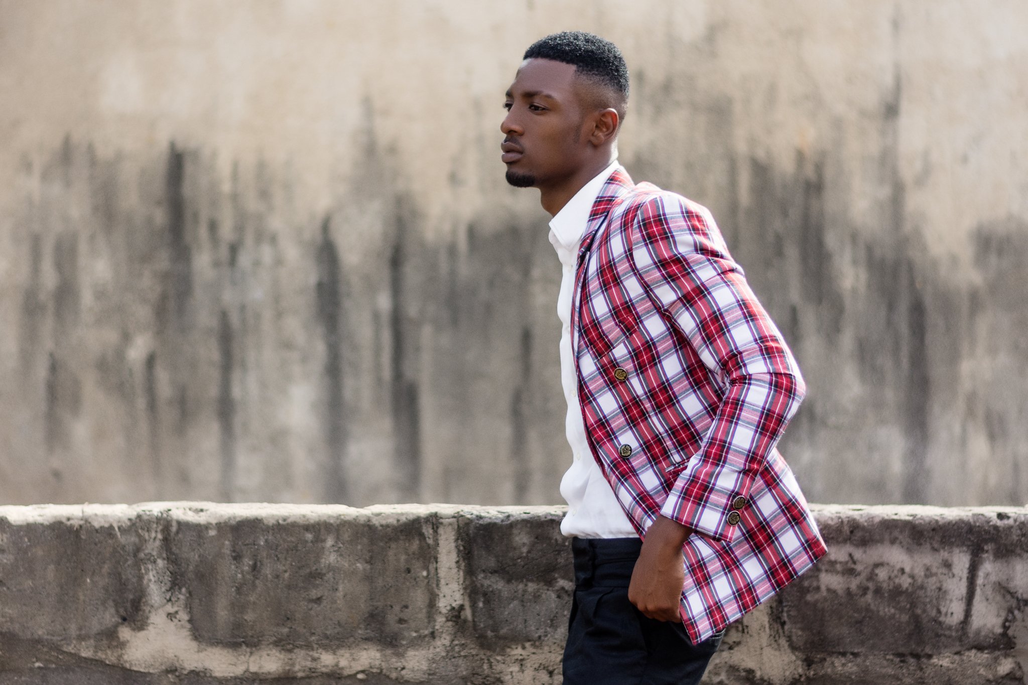 A man with a fashionable haircut wearing a red plaid blazer over a white shirt and black pants.