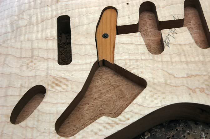 I now do the electronics, pickups, jack plate and tremolo routs. The tremolo is only one pass, the wood is only 1/8” thick here, so buzzzzz and it’s done. The other routs are done in 2 stages. First pass takes 3/8th out, and the second, the remaining 3/8th to give me a depth of 3/4 inch. Here you can see everything is the same depth. I have removed the template, and placed a block in the bridge pickup rout. This is so I can use the inside edge of what has already been routed, to take the electronics cavity on down to 1 1/2” deep.