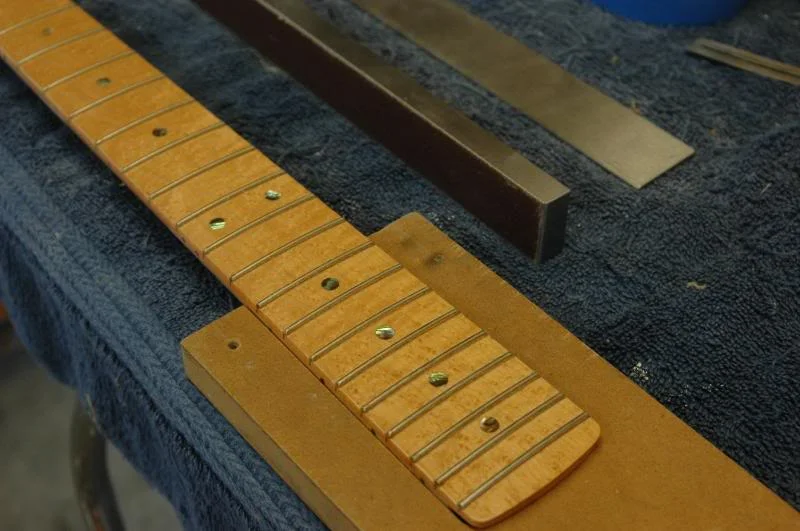 Now secure the neck whatever method you choose, I run a wood screw through one of the tuner holes into the workbench after I have pressed the heel into a neck pocket and pulled it tight.