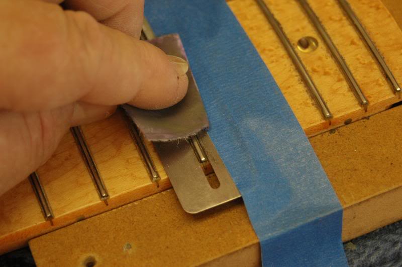  I cut ‘em in to small pieces, and give each fret a good going over, watching the reflected light off the crown to see when all the tooling marks are gone. (The tape is to hold the protector down while I took the photo with the hand that would normal