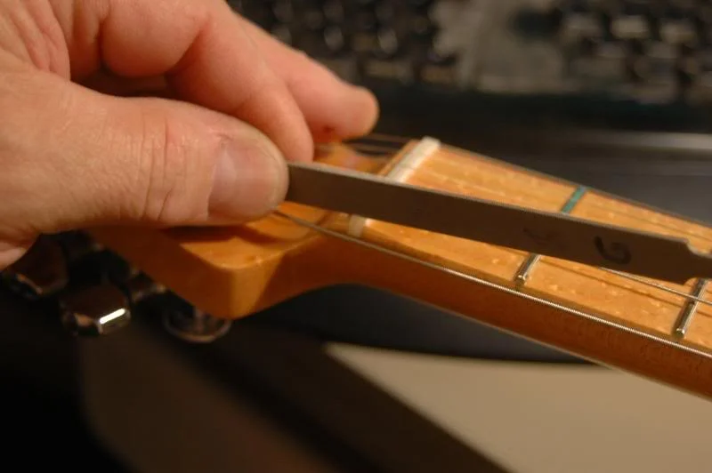 If you recall, as I was doing the assembly, I pre-slotted the nut with an approximate depth of slot, I now finish that aspect. I lift each string from the slot, give it a few swipes with the nut file, and reseat the string. I check each one leaving about 1/64th at the first fret under the first string and about 3/128ths under the 6th. Unplugged, I pluck each string, you will be able to hear if there is any fret buzz, or the dreaded “citar” sound.