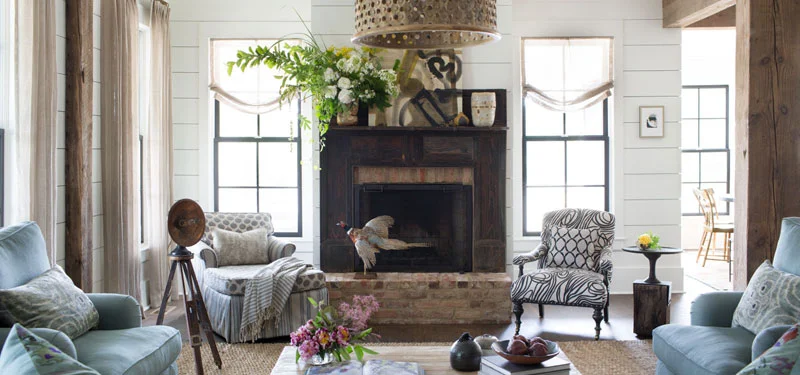 Picture of a living room designed by CLOTH & KIND in Athens, GA with white walls, light blue chairs, black and white chairs, and a brick fireplace. Text on the image reads "Modern Farmhouse".