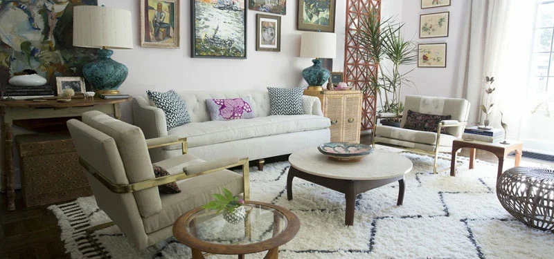 Picture of a living room designed by CLOTH & KIND in Athens, GA with white and beige chairs and sofa, white and blue patterned rug, wood and glass side tables, art filled walls, and teal lamps. Text on the image reads "Five Points Tudor Cottage".
