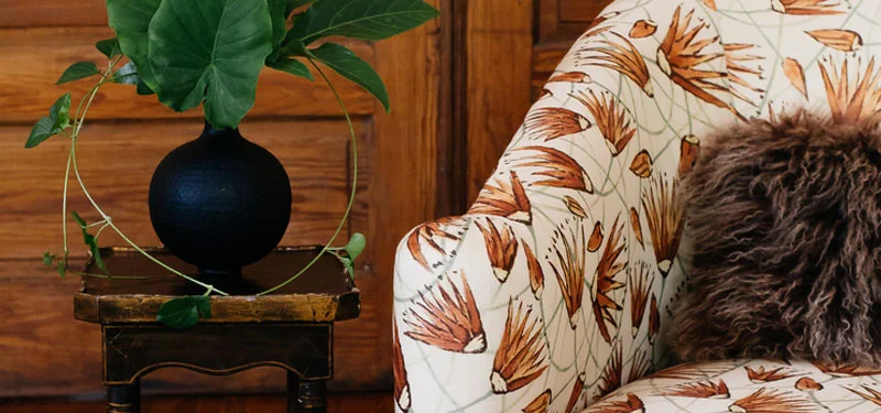 Picture of a sitting area designed by CLOTH & KIND in Athens, GA with a wood paneled wall, chair with red flower fabric, an antique side table with a black vase on top. Text on the image reads "Cobbham Victorian".