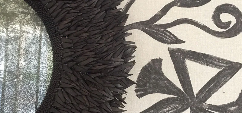 Picture of a master bedroom designed by CLOTH & KIND in Athens, GA with a close up of a circle mirror that has black petals around it, and a black and white wallpaper with leaves. Text on the image reads "Serenbe Showhouse".