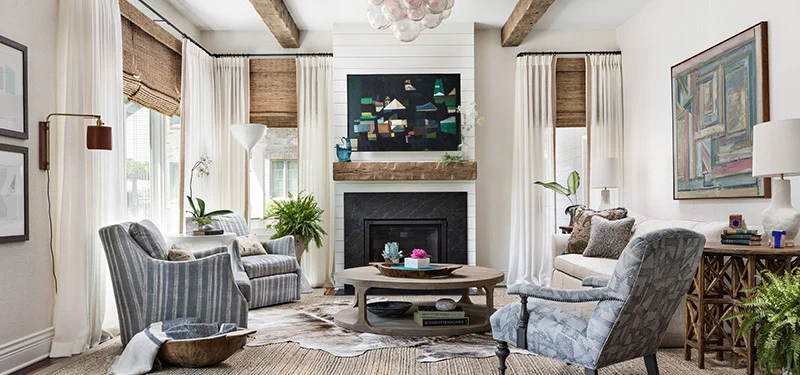 Picture of a living room designed by CLOTH & KIND in Ann Arbor, MI with an animal skin rug, light blue patterned chairs, a beige couch, a wooden coffee table, modern art and glass bubble light fixture. Text on the image reads "Orchard Au Courant".
