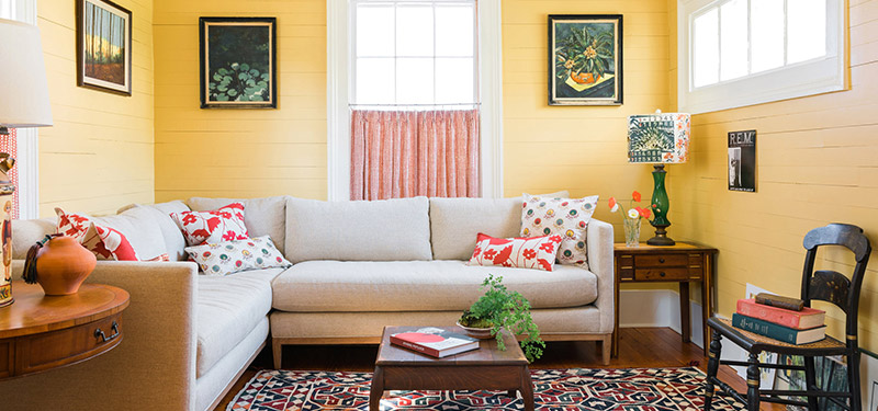 Picture of a living room designed by CLOTH & KIND in Athens, GA with yellow walls, wood side tables, and a beige sectional couch. Text on the image reads "Historic Meigs Street".