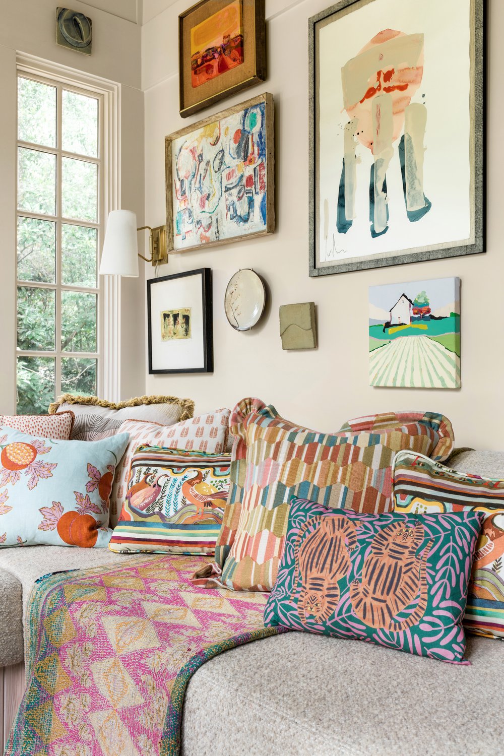  Close up photo of a sitting room designed by CLOTH &amp; KIND with a built-in L shaped bench covered in an assortment of colorful pillows and a gallery wall. 