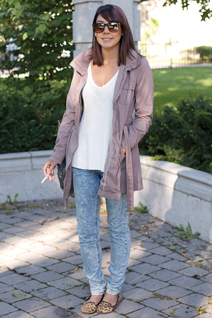 University of Toronto student enjoys a morning smoke. She is wearing a tan grey trench coat over a white top, faded blue jeans and leopard print flats.