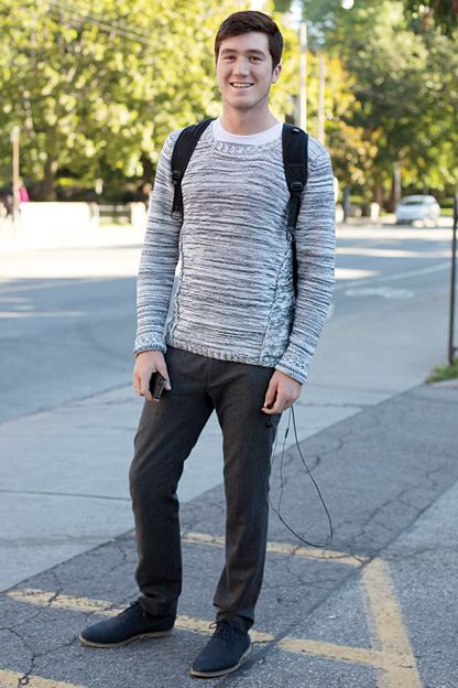 University of Toronto student wears a low scoop neck grey and white wool patterned sweater over a t-shirt, brown wool pants and blue suede oxfords