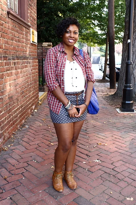 Virginia Commonwealth University student wears an open red and white plaid shirt over a white top a white polka dotted blue skirt, a brown belt and brown lace-up booties
