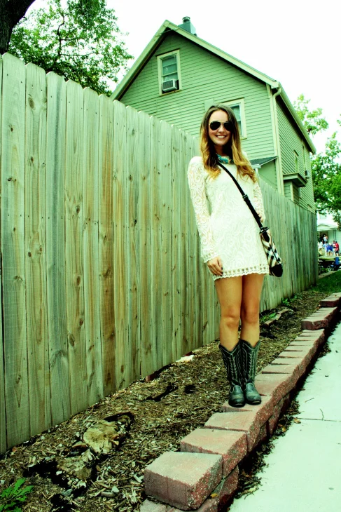 University of Kansas student wears a white long sleeved lace sleeve and trim dress with white trim black leather cowboy boots and ray ban aviators
