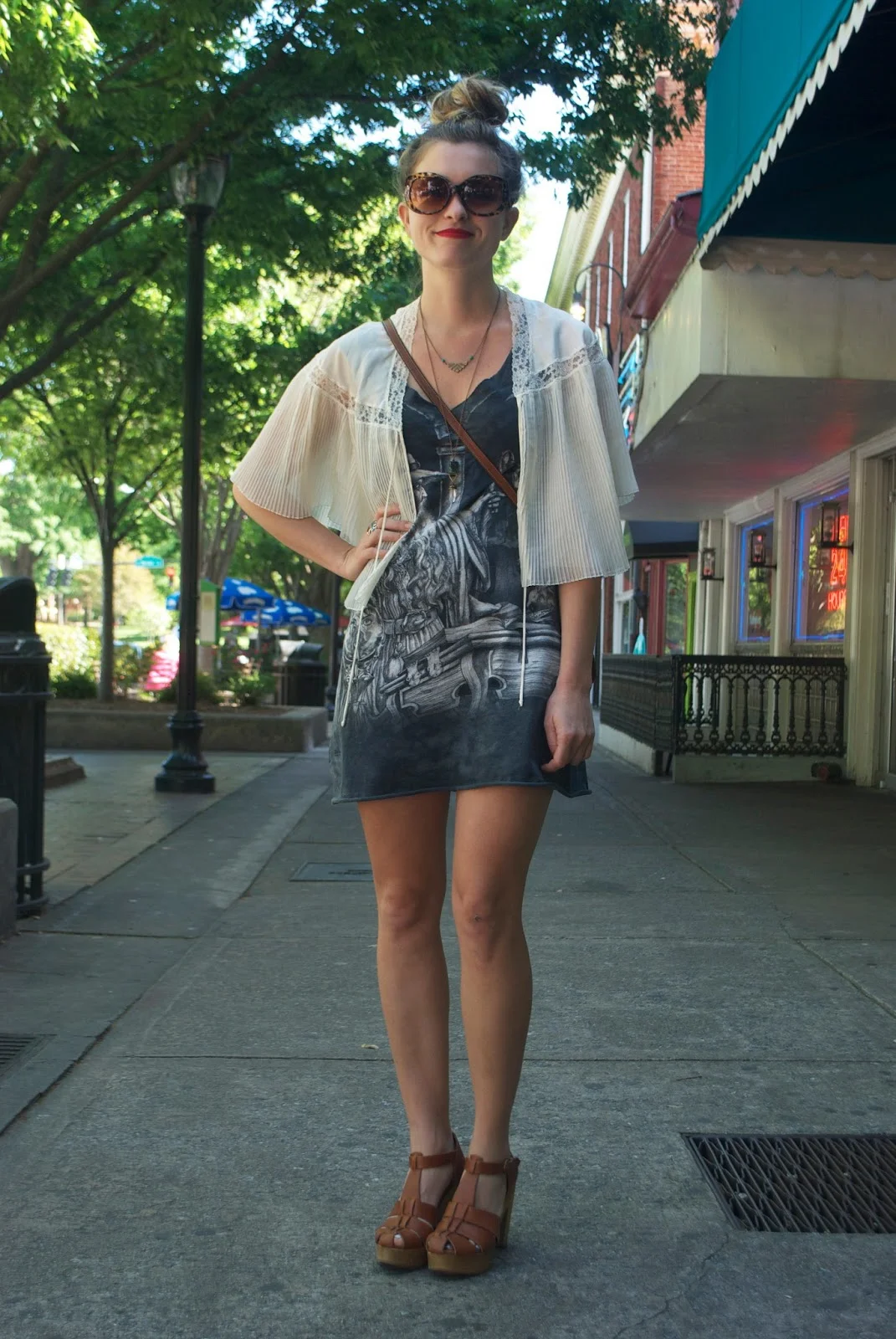 University of Georgia Student wears a dark print dress with a white cardigan and brown leather strap bootie heels