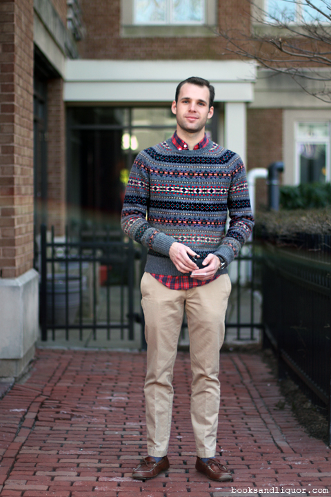 This male student wore a black grey and red fair isle patterned sweater over a red and blue plaid shirt and khaki pants, blue socks and brown leather moccasins.