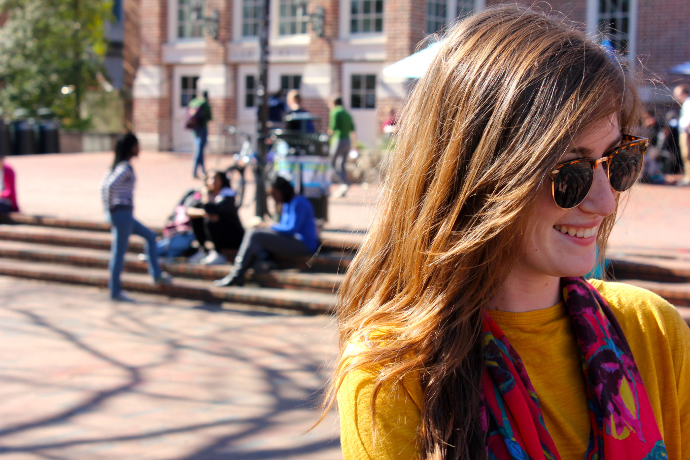 Sara C, a UNC Chapel Hill sophomore majoring in Journalism and Mass Communications wears a floral print pink/fuchsia scarf over a bright mustard yellow sweater, blue jeans and light brown suede chukka boots