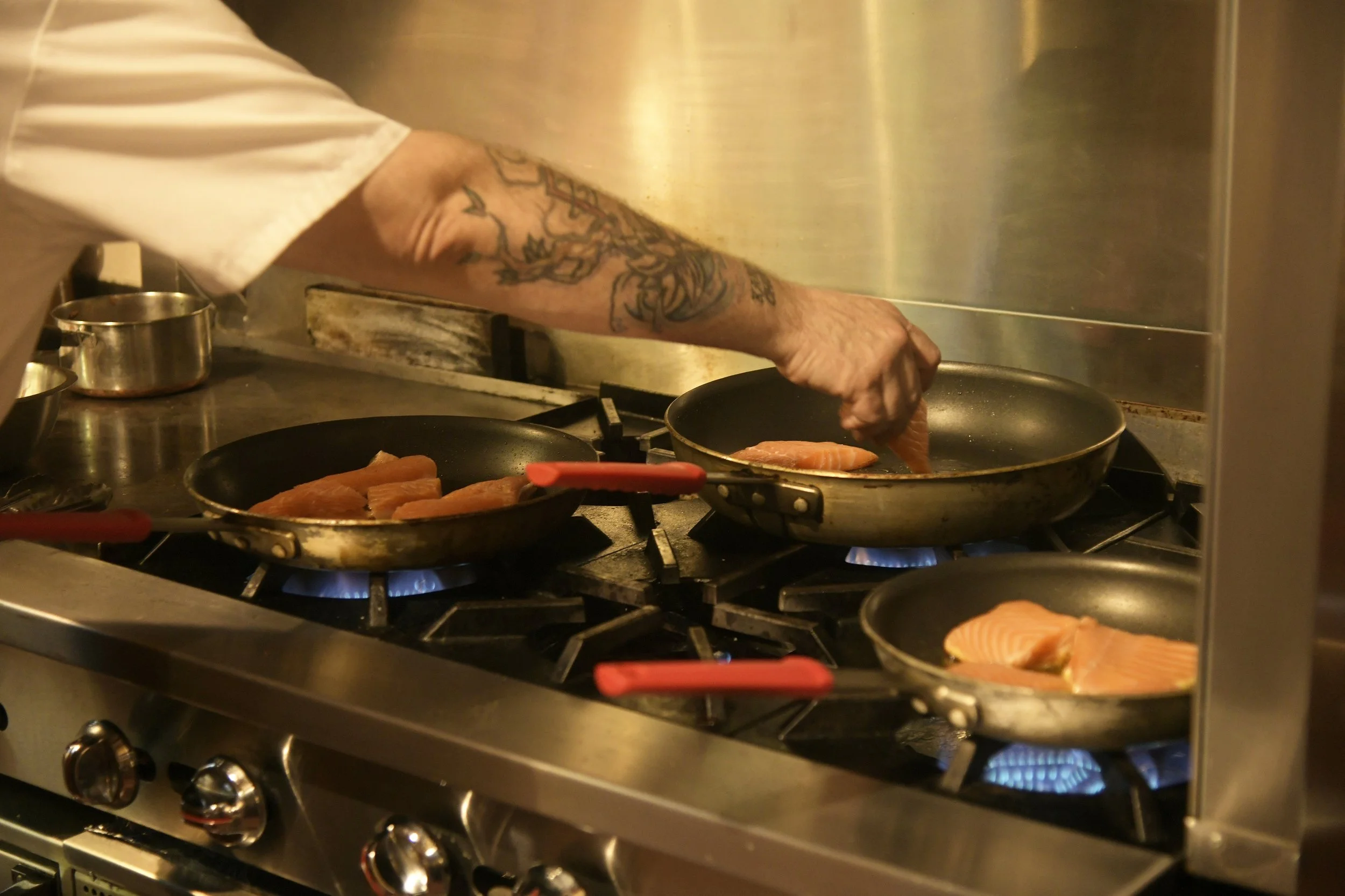 Person cooking salmon fillets in a commercial kitchen stove.