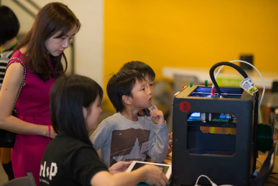 A staff guides a mother and children to the mechanics of a 3D Printer.