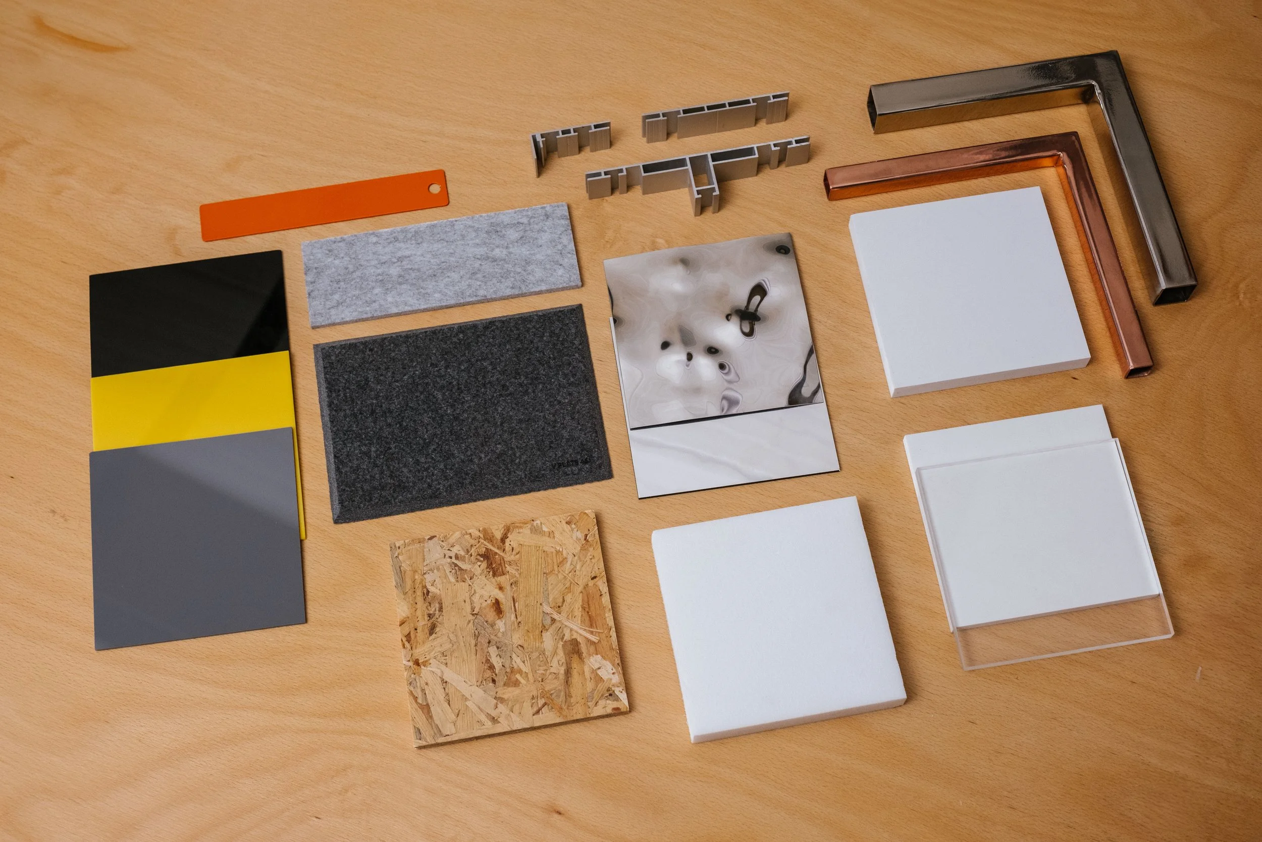 Various sample materials and color swatches arranged on a wooden table, including metal, glass, fabric, and plastic samples in different shapes and colors.