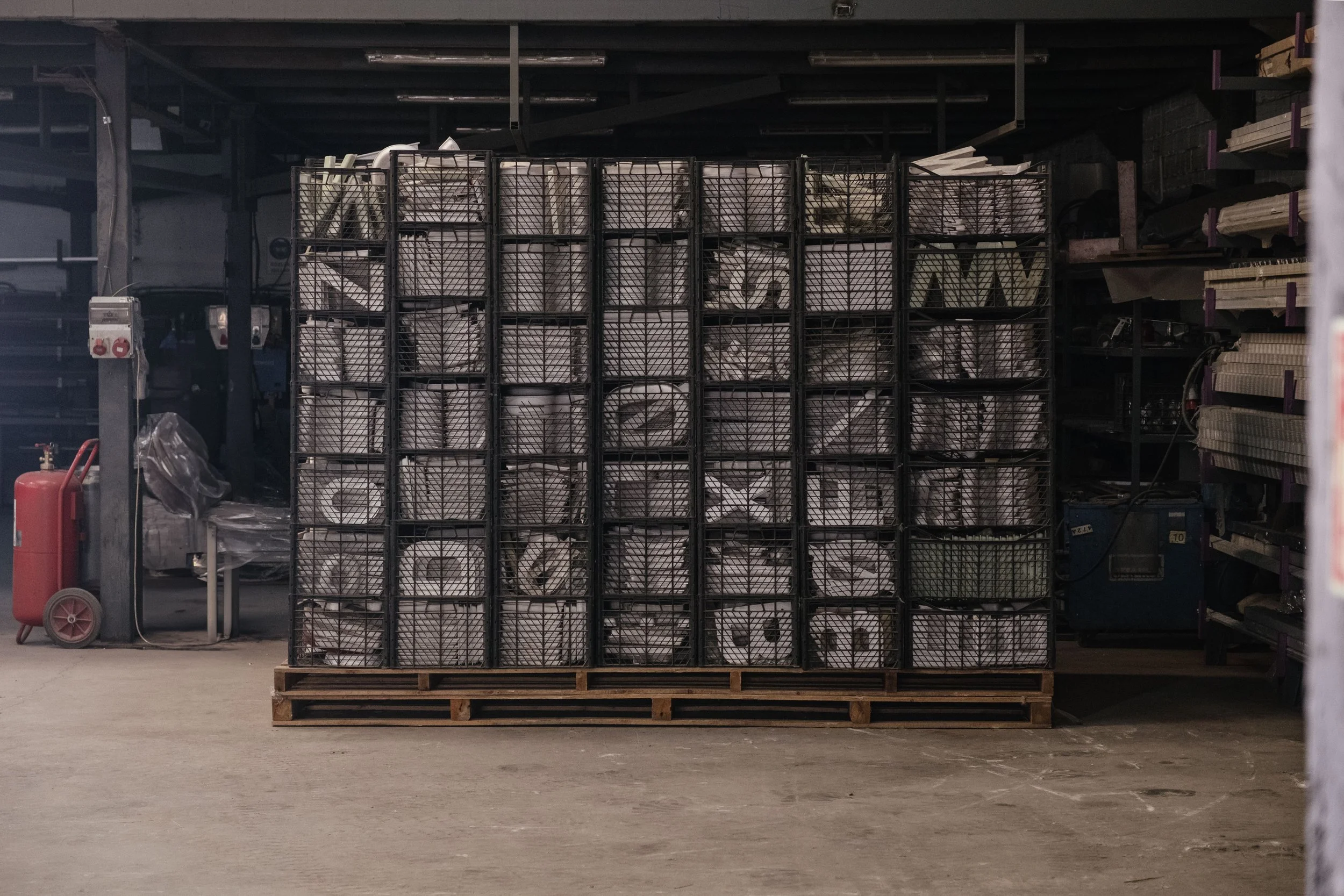 A pallet stacked with multiple metal wire baskets filled with rolled white paper or fabric in a warehouse or storage space.